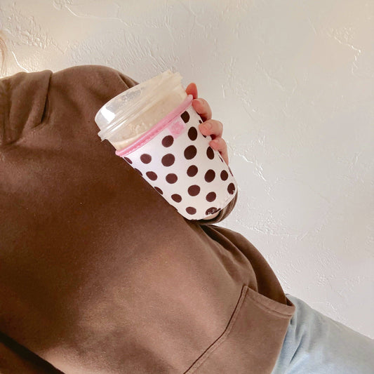 Person holding a polka dot cup against a plain background