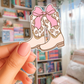 Cartoon boots with a pink bow held by a hand in front of a bookshelf.