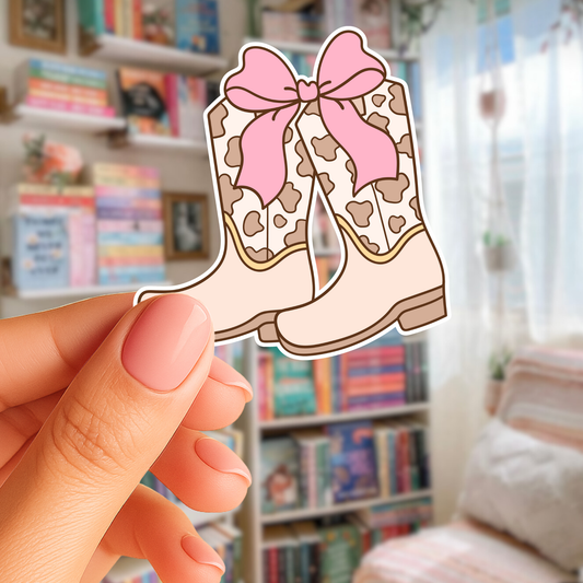 Cartoon boots with a pink bow held by a hand in front of a bookshelf.