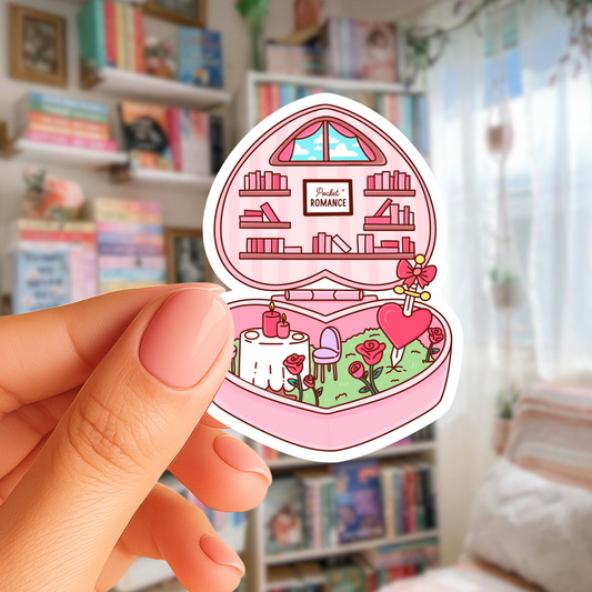 Sticker of a pink jewelry box with a scene inside, held by a hand in a room with bookshelves.