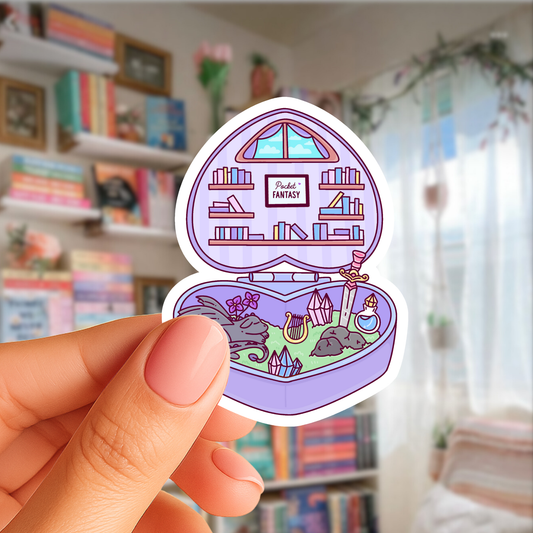 Hand holding a colorful sticker of a fantasy scene with books and a castle in a room with bookshelves.