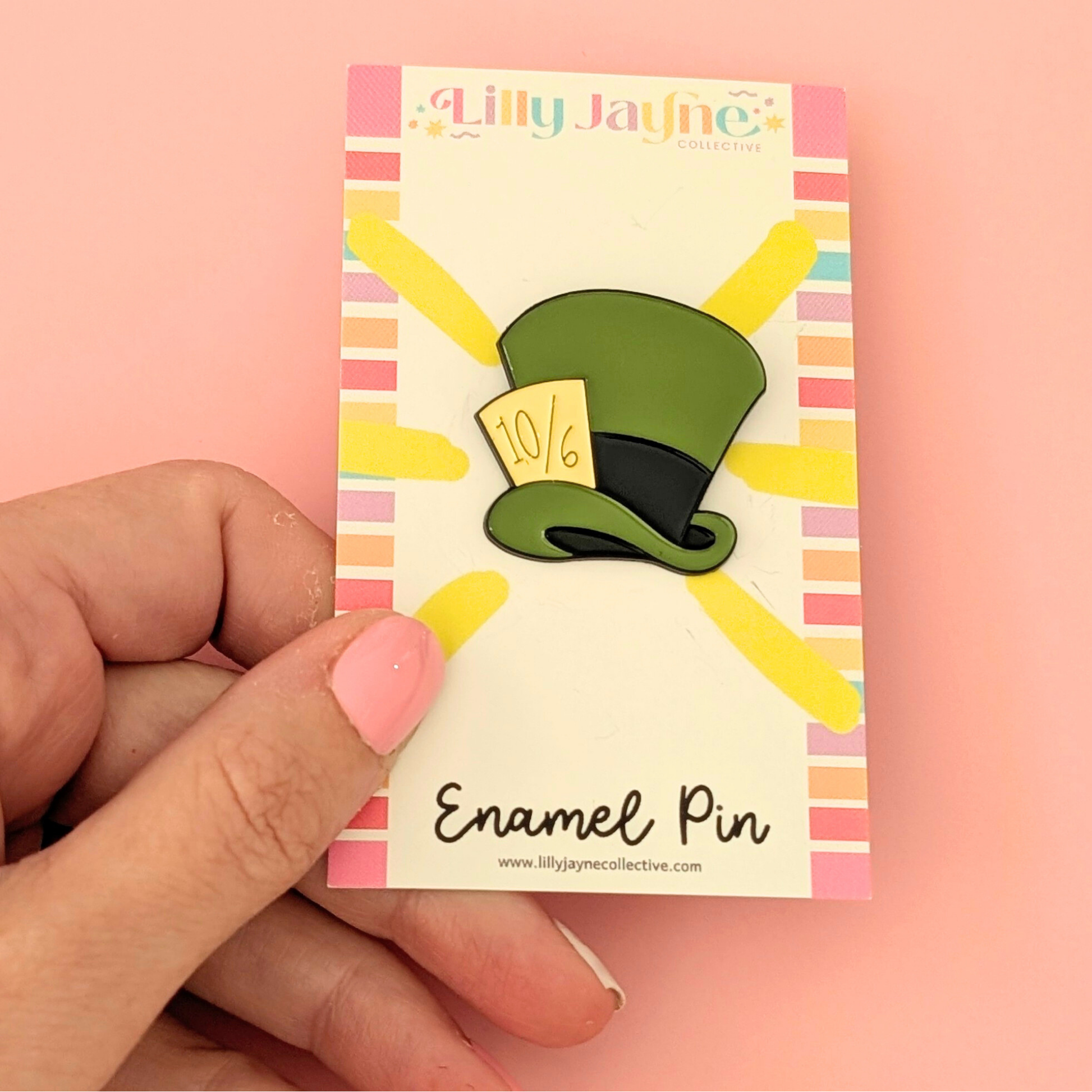 Enamel pin on a card held by a hand against a pink background