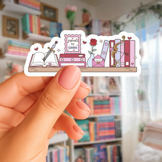 Hand holding a sticker with a design of books and a heart in a room with bookshelves.