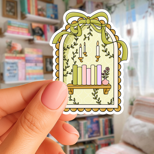 Hand holding a decorative sticker with candles and plants against a blurred bookshelf background