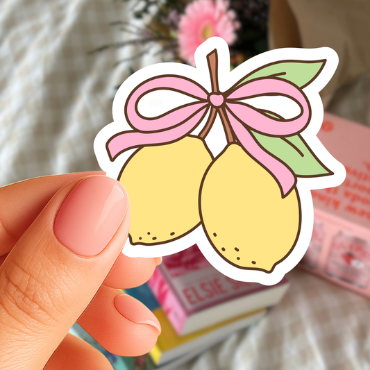 Hand holding a sticker of two lemons with a pink bow against a blurred background