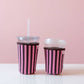 Two cups with pink and black striped sleeves on a white surface with a pink background
