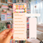 Colorful bookmark with reading log questions held by a hand in front of a bookshelf.