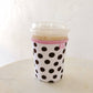Coffee cup with polka dot sleeve and pink trim on a white surface