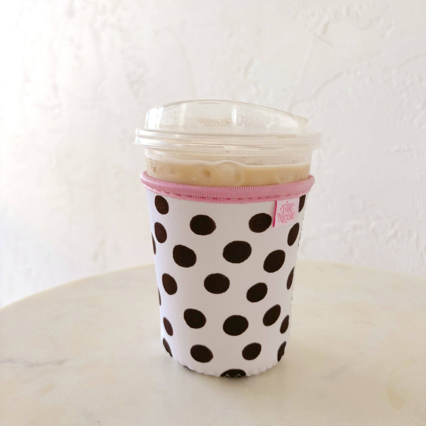 Coffee cup with polka dot sleeve and pink trim on a white surface