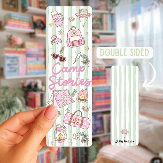 Double-sided bookmark with 'Camp Stories' design held by a hand in front of a bookshelf.