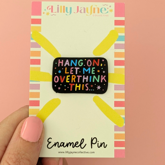 Enamel pin with 'Hang on, let me overthink this' text on a colorful card held by a hand.