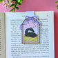 Decorative bookmark with a dragon illustration on an open book against a pink background.