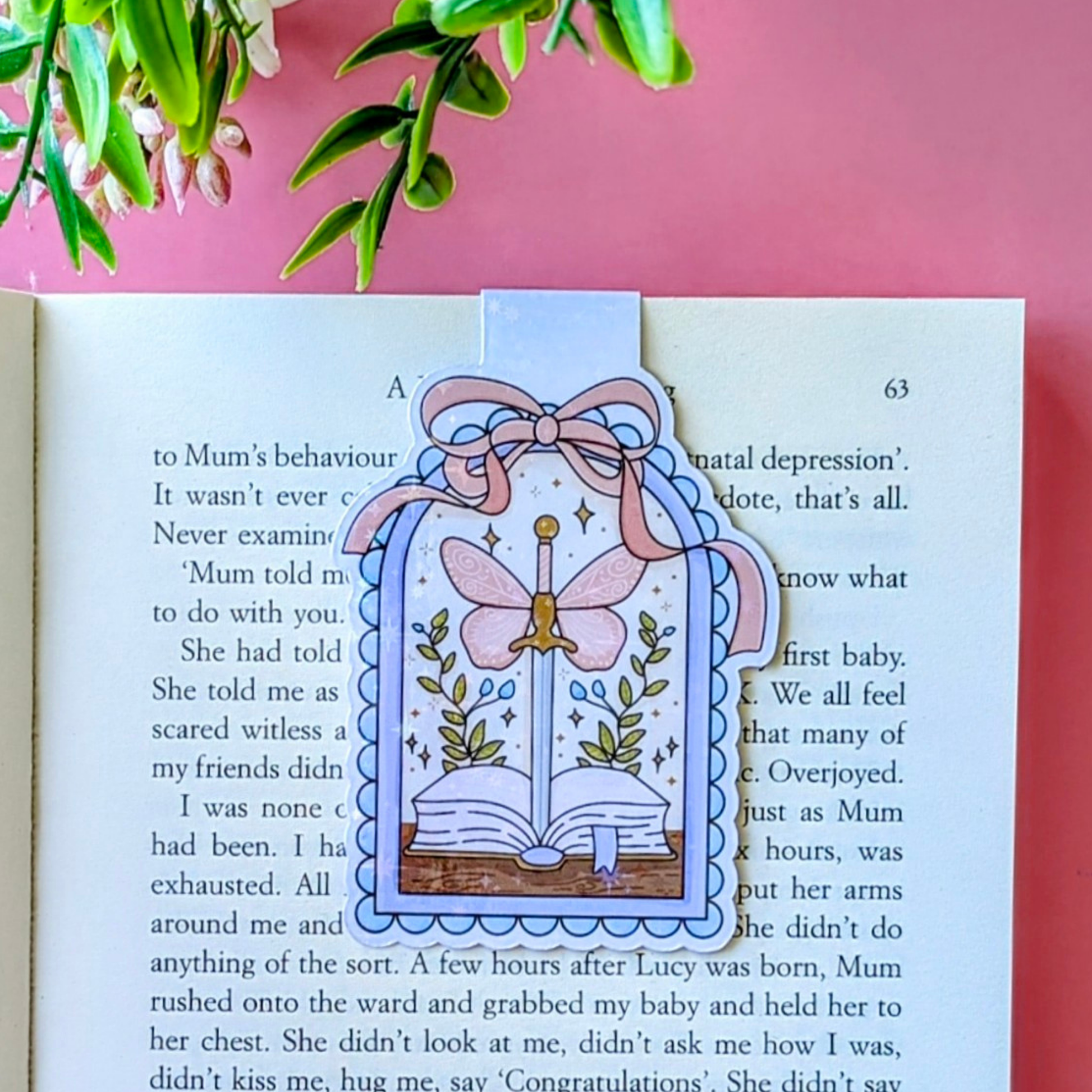 Decorative bookmark with a butterfly design on an open book against a pink background