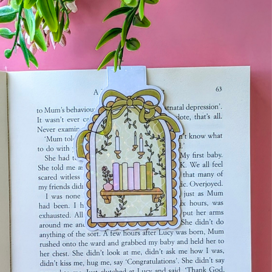Decorative bookmark with a candle design on an open book against a pink background
