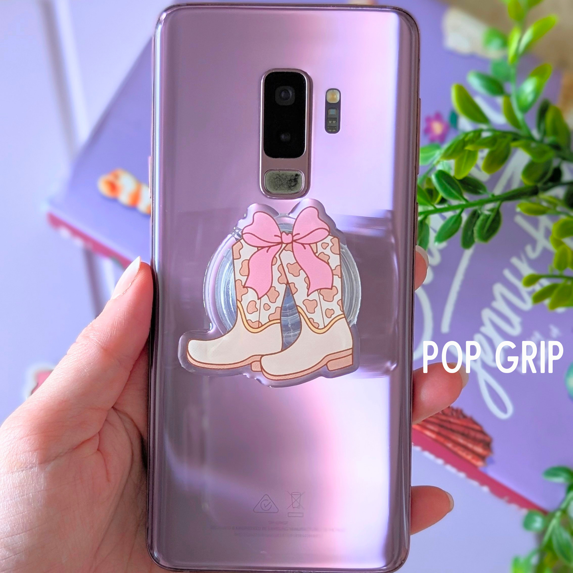 Phone case with cowboy boots and a bow design held by a hand, with 'POP GRIP' branding.