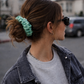 Person with a teal scrunchie in their hair, wearing sunglasses and a denim jacket.