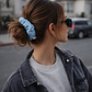 Person with a blue scrunchie in their hair, wearing sunglasses and a denim jacket.