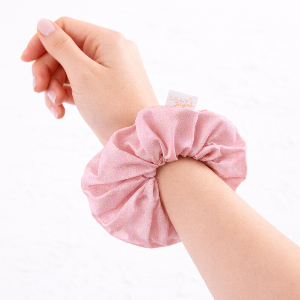 Pink scrunchie on a wrist with a white background