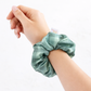 Hand wearing a green scrunchie on a white background