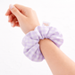 Hand wearing a purple checkered scrunchie on a white background