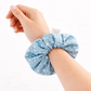 Hand wearing a blue scrunchie with white floral pattern on a white background
