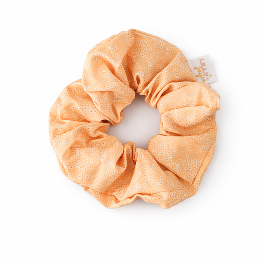 Orange scrunchie with a brand tag on a white background