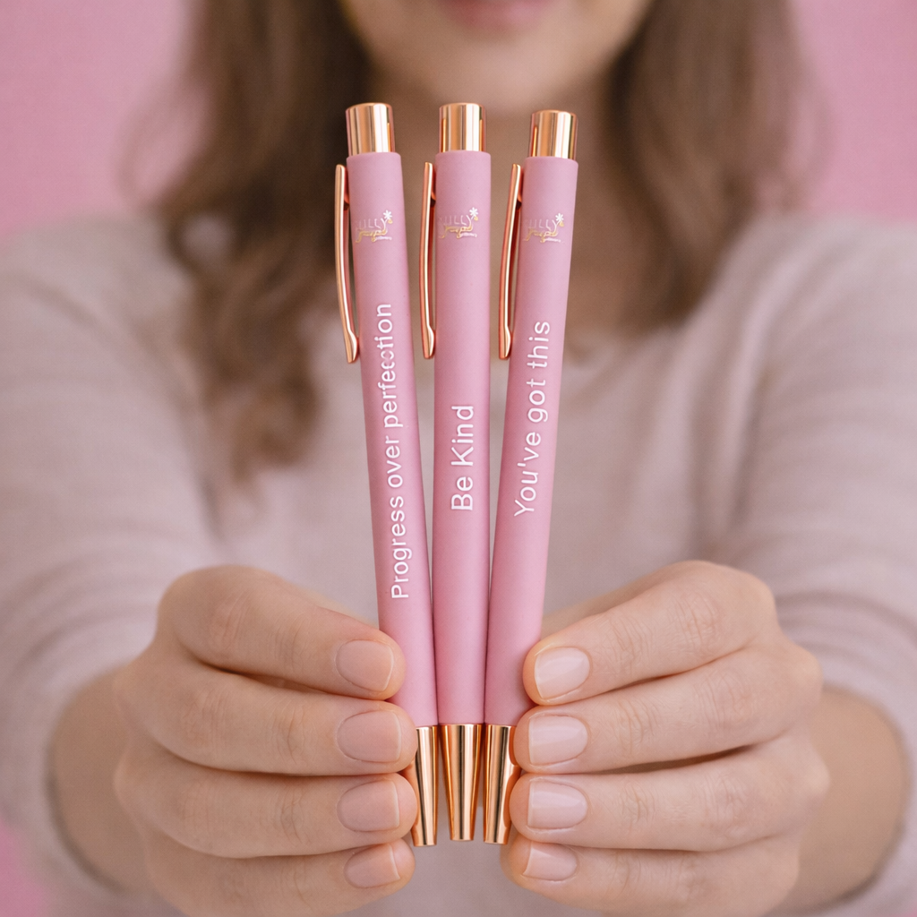 Person holding three pink pens with motivational quotes, against a pink background