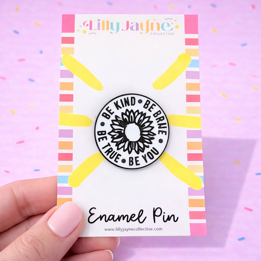 Enamel pin with motivational quote on a colorful card held by a hand against a pink background