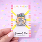 Enamel pin with 'Grow Positive Thoughts' design on a colorful card, held against a pink background with polka dots.