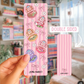 Pink packaging with cartoon designs held by a hand, with a blurred background of books and decor.