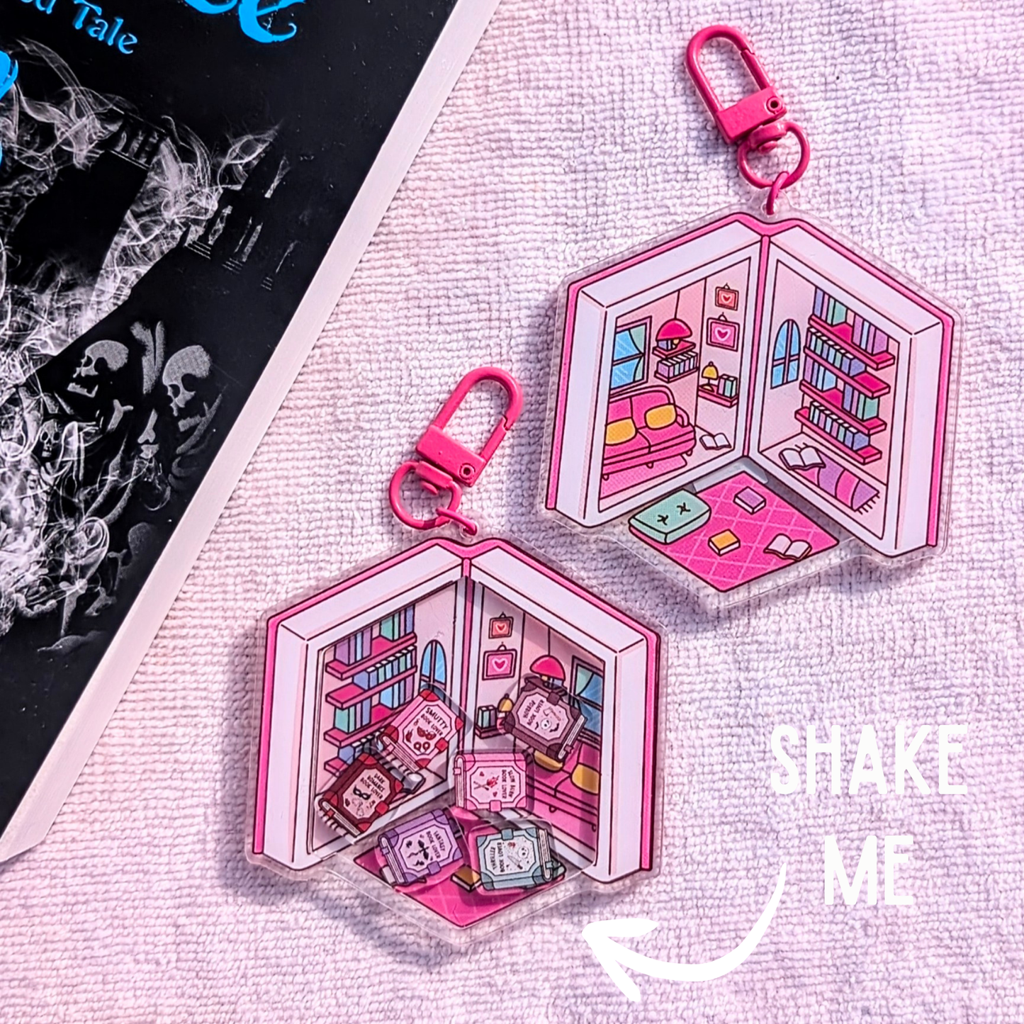 Pink keychain with a miniature scene of a room with books and a character, on a textured surface.