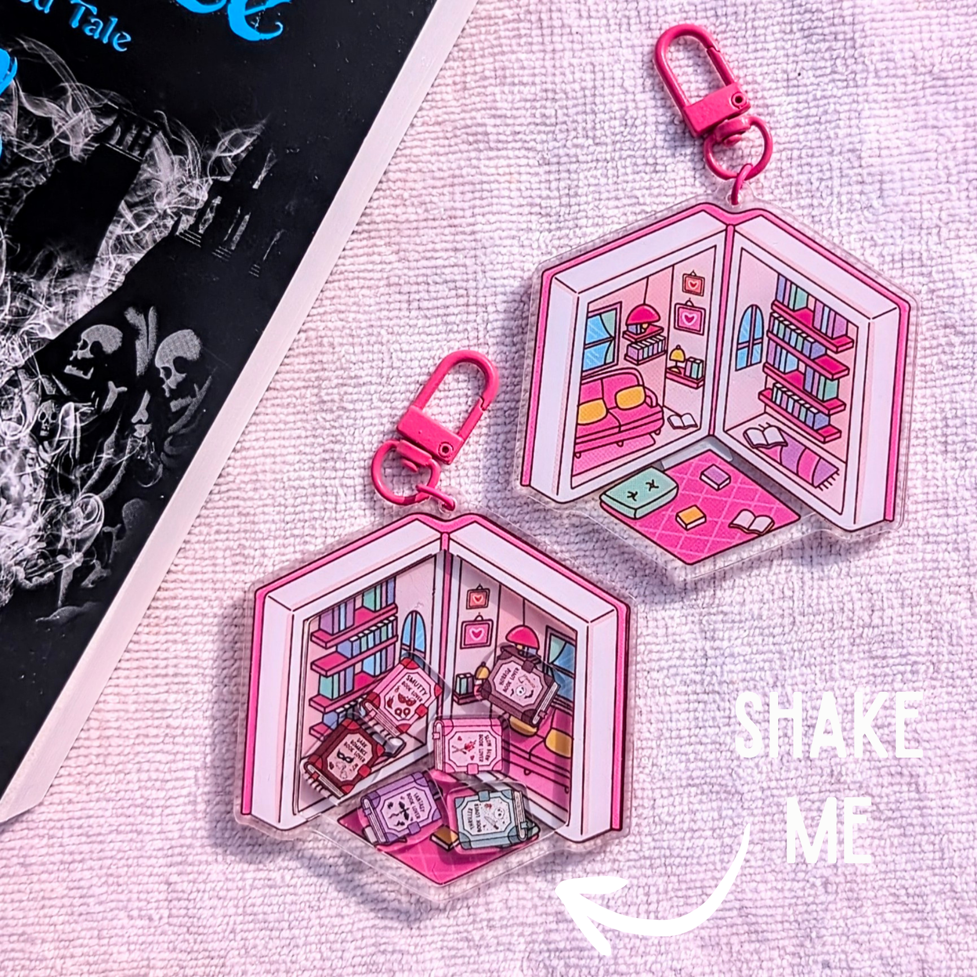 Pink keychain with a miniature scene of a room with books and a character, on a textured surface.