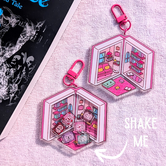 Pink keychain with a miniature scene of a room with books and a character, on a textured surface.