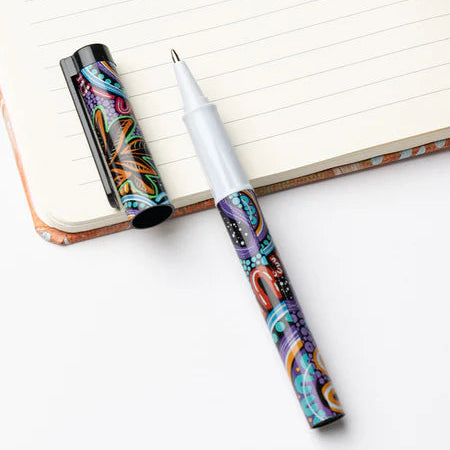 Colorful pen with artistic design on a white surface next to an open notebook.