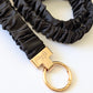Black scrunchie keychain with gold clasp on a white background