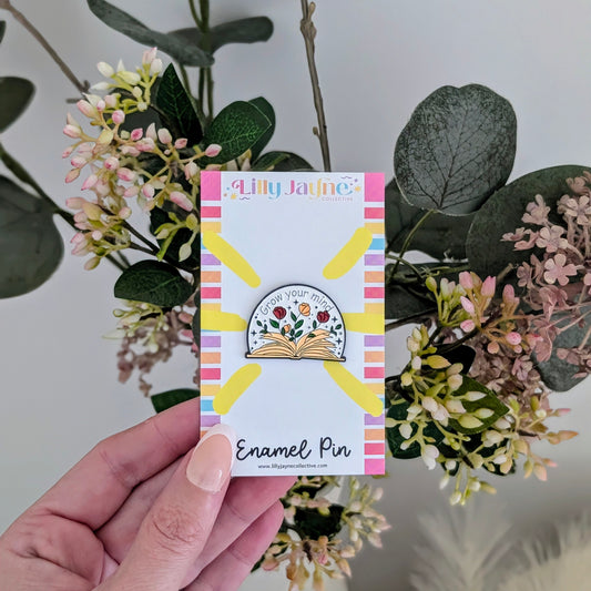 Enamel pin on a card held in front of floral decorations