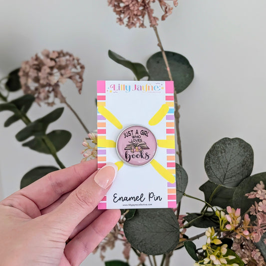 Hand holding a card with an enamel pin featuring a sun design and text, against a floral background.