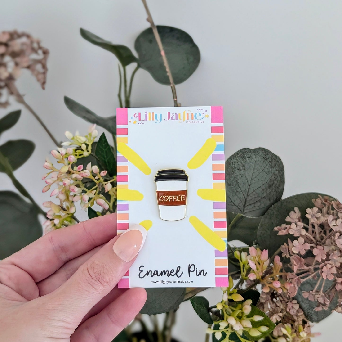 Enamel pin packaging held by a hand with plants in the background