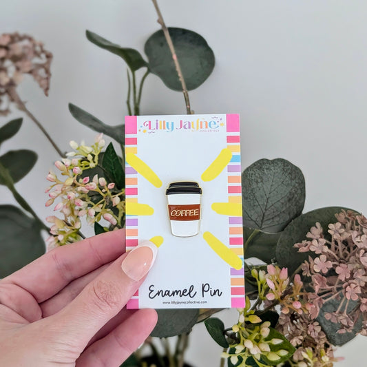 Enamel pin packaging held by a hand with plants in the background