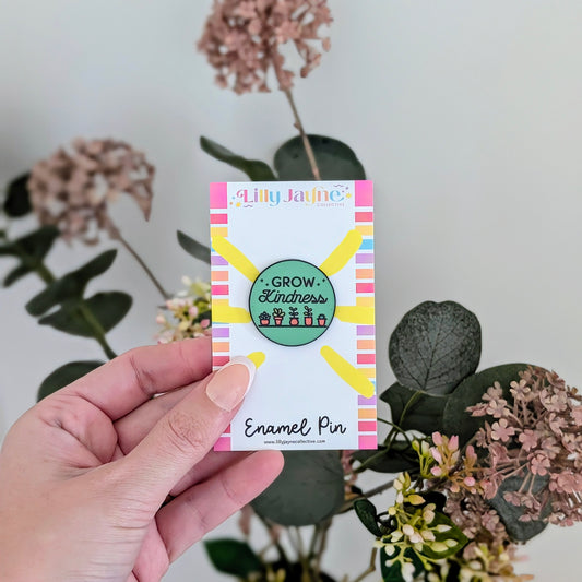 Hand holding a card with an enamel pin design featuring plants and 'Lilly Jayne' branding.