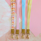 Four colorful lanyards with floral and checkered patterns on a pink and white marble background.