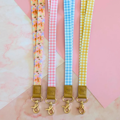 Four colorful lanyards with floral and checkered patterns on a pink and white marble background.