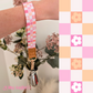 Three colourful fabric wristlet keychains with gold hardware and tan leather ends, featuring pink gingham daisy, blush polka dot stripe, and retro orange checker floral patterns, laid on pastel notebooks with floral accents – Lilly Jayne Collective.