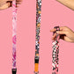 Lanyard with colorful pattern held by hands against a pink background