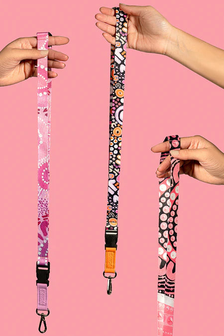 Lanyard with colorful pattern held by hands against a pink background