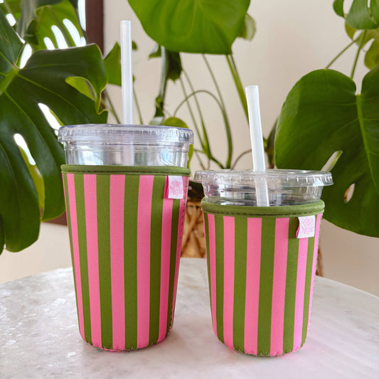 Two striped cups with green and pink pattern on a table with plants in the background