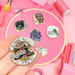 Collection of sewing-themed pins on a pink background with sewing supplies.