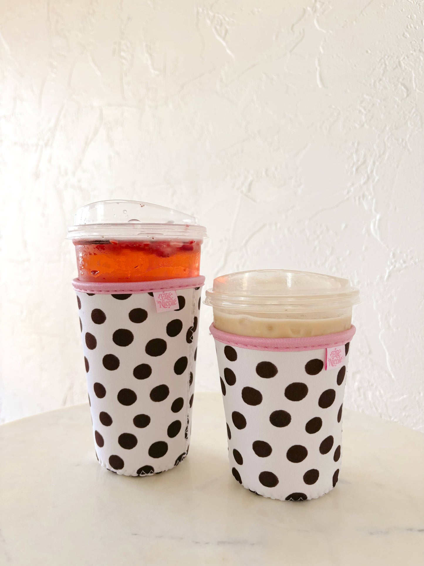 Two polka dot cups with pink lids on a white surface.