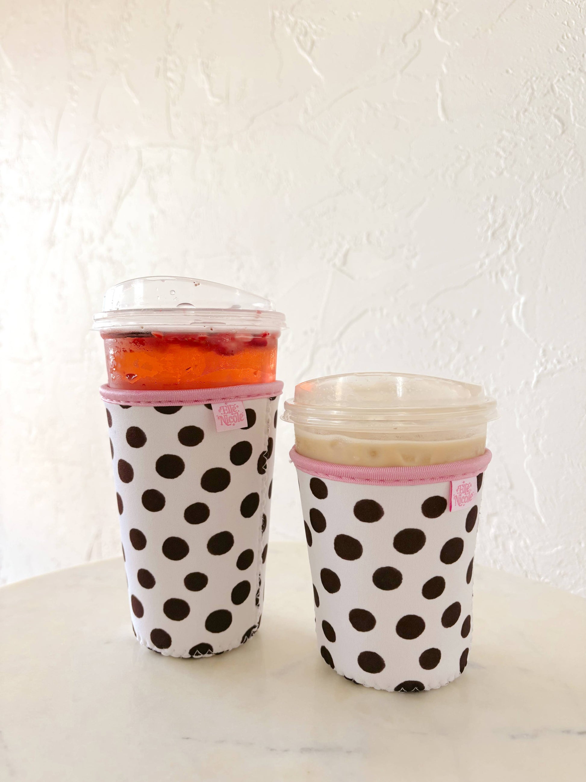 Two polka dot cups with pink lids on a white surface.