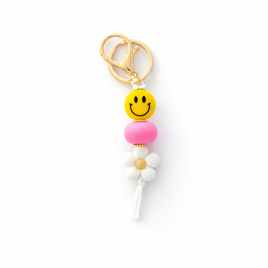 Keychain with smiley face, pink bead, and white flower on a white background